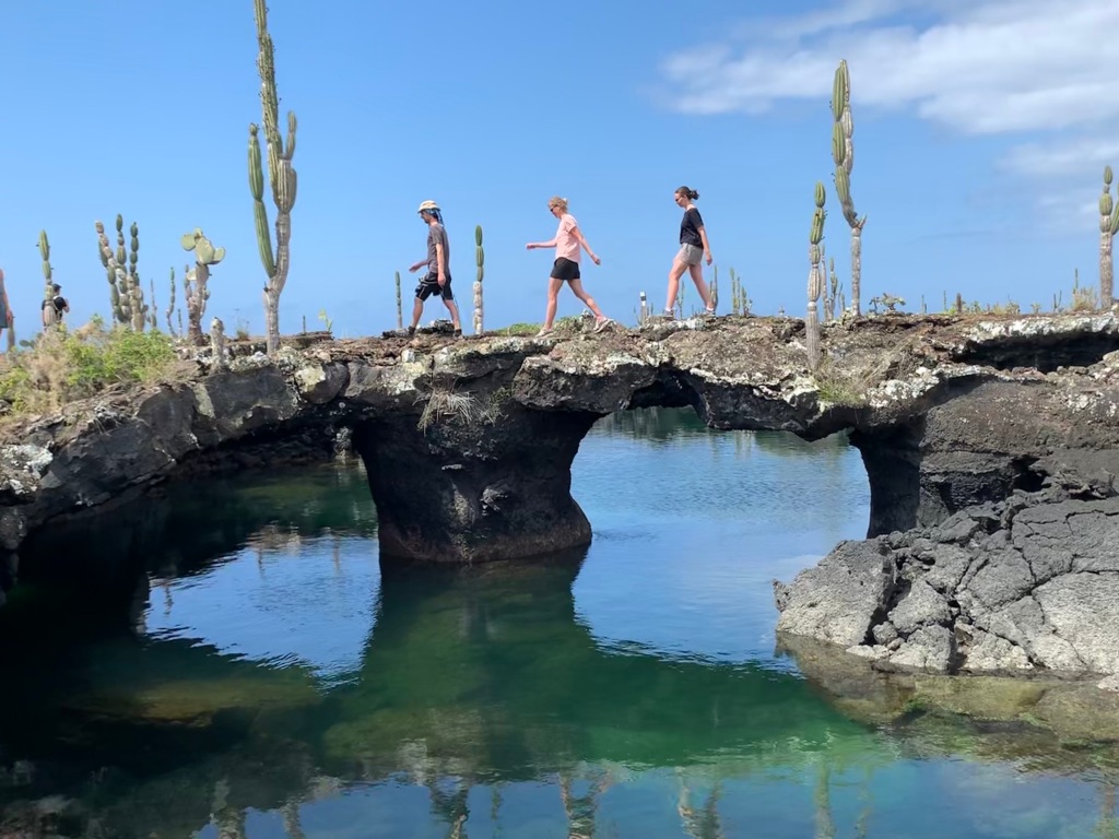 photo-of-three-people-crossing-natural-rock-bridge-tintoreras-galapagapos